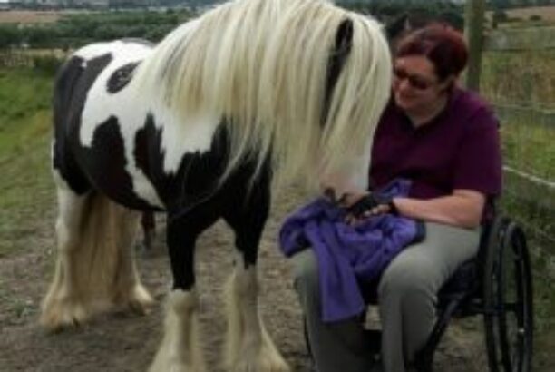 Dark haired lady in a wheelchair in a field with a black and white horse